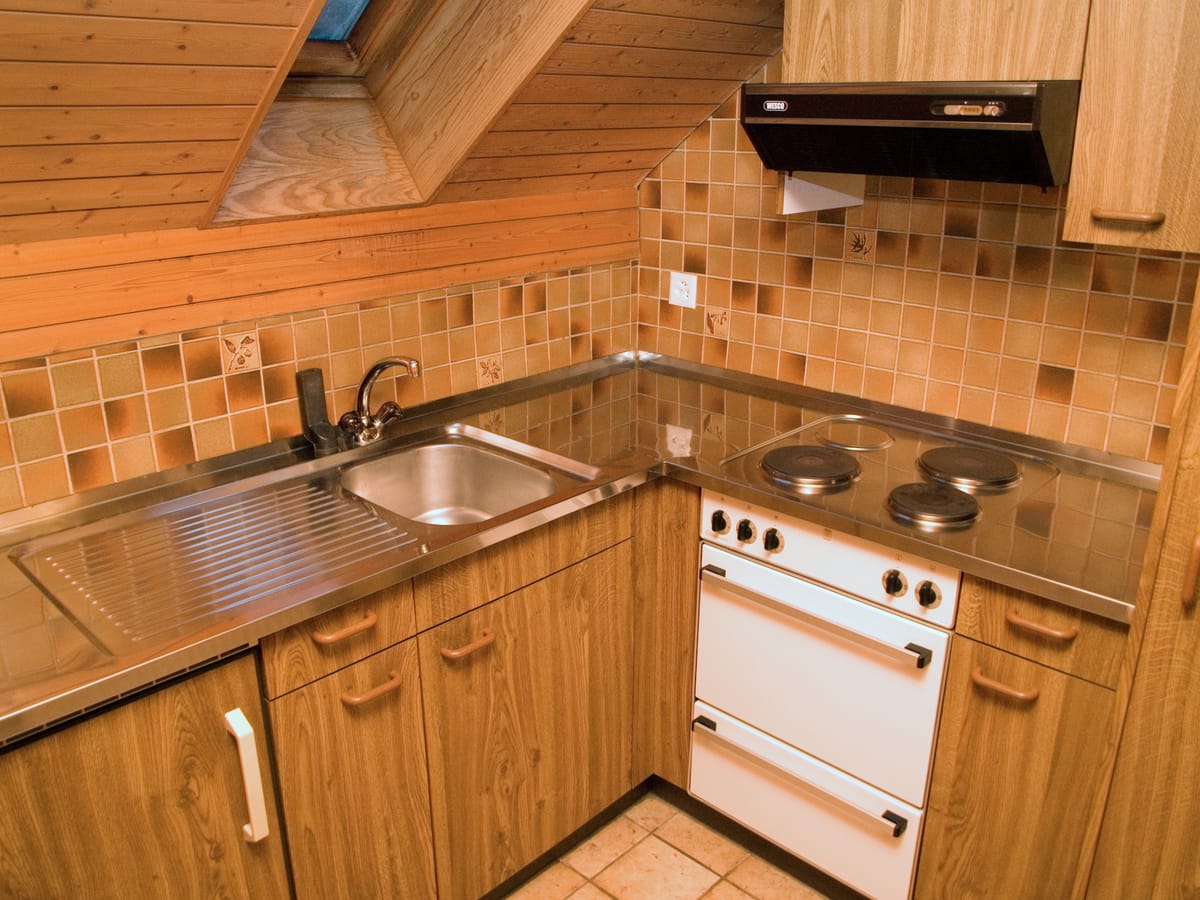 A small kitchen with wood-fronted cupboard doors and drawers below a hob and extractor hood