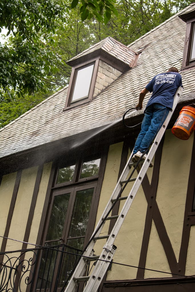 Someone on a ladder flushing leaves out of a house gutter with a hose