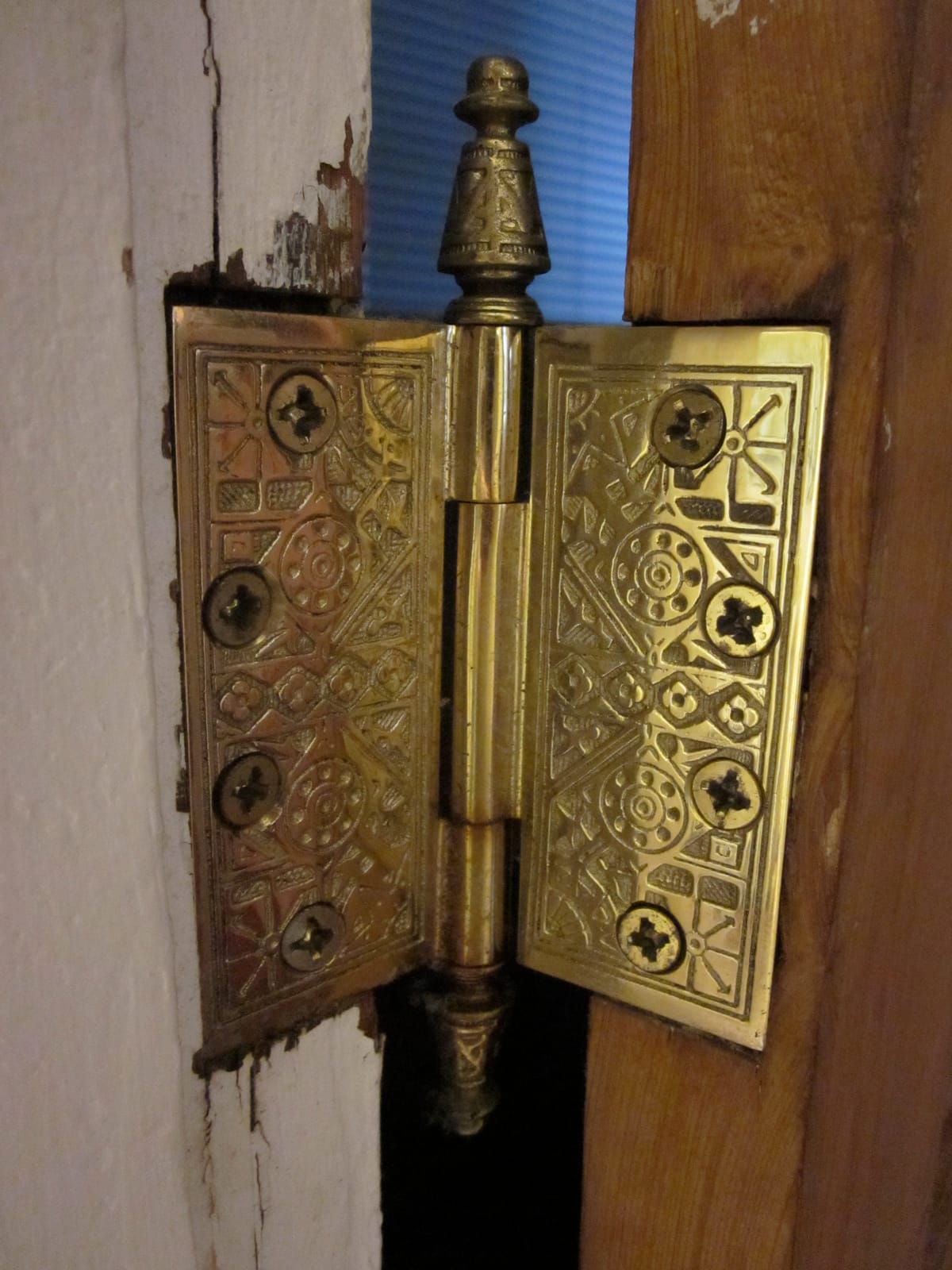 An ornate brass butt hinge on an interior door frame, with the pin, barrel and knuckles clearly visible