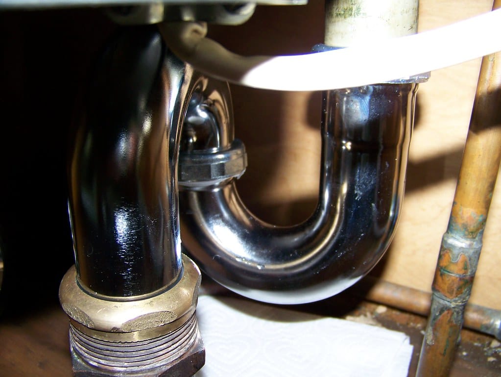 A chrome P-trap under a bathroom basin, with the slip-joint nuts visible