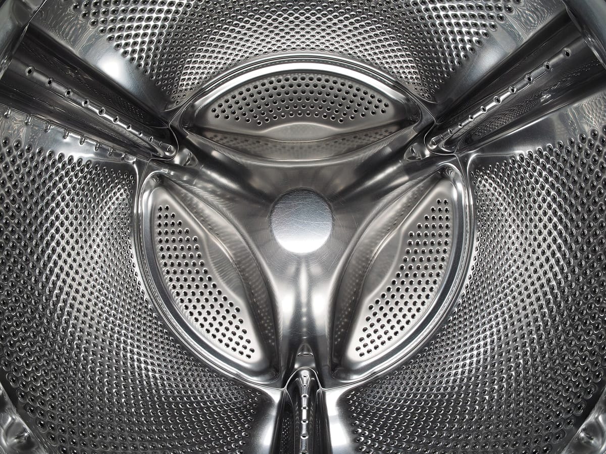 The stainless steel interior of a modern front-loading washing machine drum, with its perforated wall and three raised paddles.