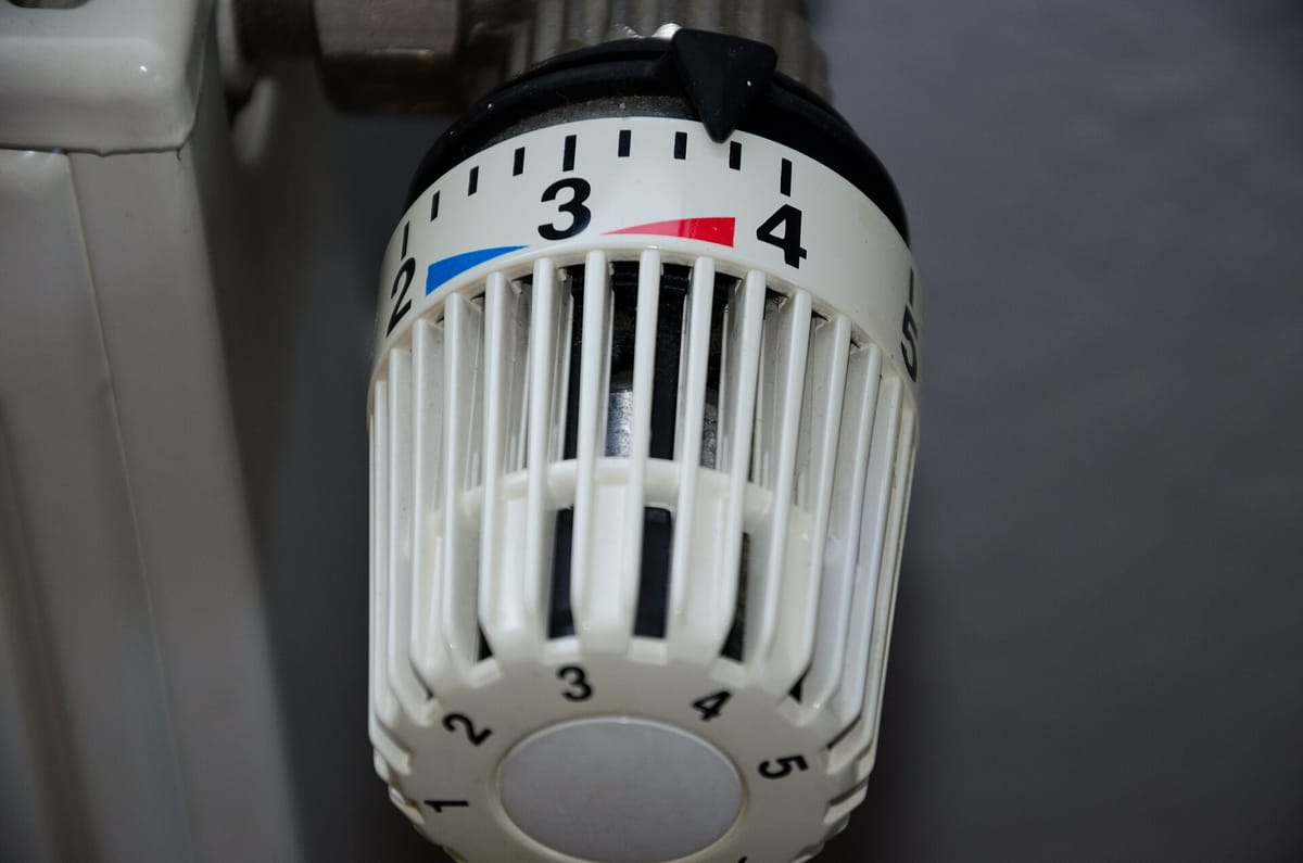Close-up of a white thermostatic valve head on a radiator, its dial numbered 1 to 5 and turned to just above 3.