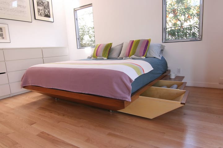 A low platform bed in a small room with a wide storage drawer slid out from underneath it