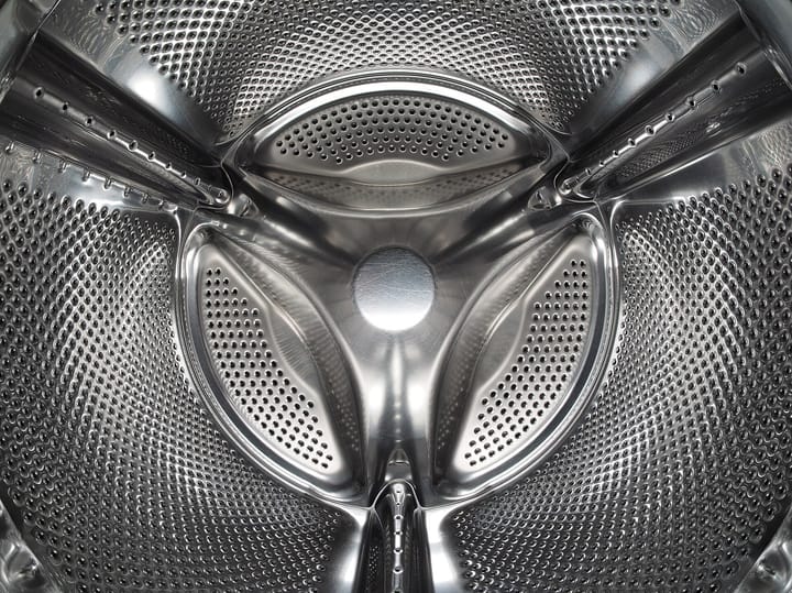 The stainless steel interior of a modern front-loading washing machine drum, with its perforated wall and three raised paddles.