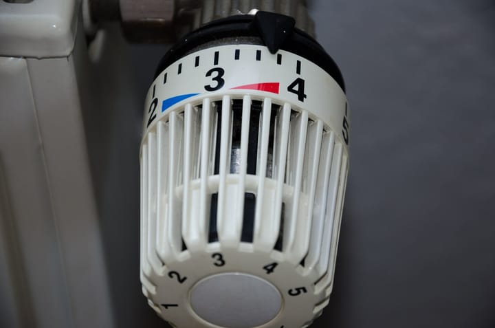 Close-up of a white thermostatic valve head on a radiator, its dial numbered 1 to 5 and turned to just above 3.